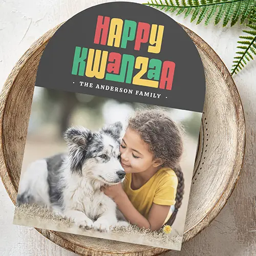 A personalized arched-top holiday card for Kwanzaa featuring a dark charcoal gray header with large red, green, and gold geometric 'HAPPY KWANZAA' text, a custom family name area, and a large custom photo area below.