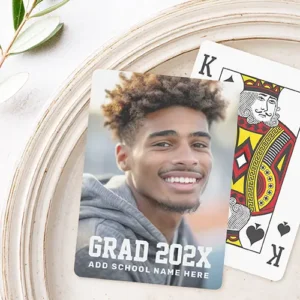 A rectangular custom playing card with rounded corners, featuring a full-bleed custom photo template. Layered over the bottom section of the photo is bold white typography reading "GRAD 202X" in a varsity block font, with a secondary text line underneath for a custom school name.