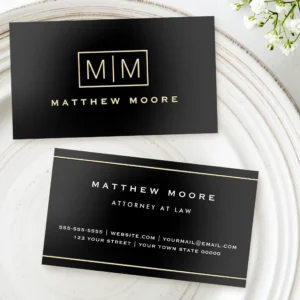 Elegant foil monogram name & borders black business cards Front and back view of a horizontal black business card. The front features a gold foil rectangle enclosing a side-by-side monogram divided by a vertical line, with name text in gold below. The back has parallel gold foil border lines along the top and bottom edge, framing clean centered white text for name, title, phone, website, email, and office address.