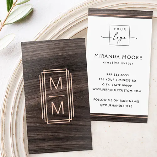 A two-sided vertical business card template. The front features a full-bleed dark wood background centered with a multi-bordered metallic rose gold foil frame enclosing two stacked letters. The reverse side features top and bottom dark wood accent bars with metallic foil lines and a white central text area with placeholders for a logo and contact information.