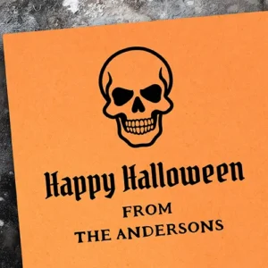 A high-contrast Halloween rubber stamp design. The top features a detailed skull illustration. Centered below is "Happy Halloween" in a gothic blackletter font, followed by all-caps serif text placeholders reading "FROM" and a customizable name field suitable for family or business details.