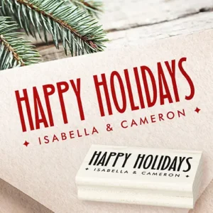 An ink rubber stamp featuring tall, elongated condensed uppercase letters spelling Happy Holidays above a widely spaced second line of custom text flanked by four-point diamond starburst symbols.