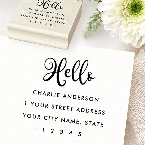 A custom return address rubber stamp. The top section showcases a large handwritten calligraphic script word reading "Hello". Centered below are four lines of clean, all-caps sans-serif text placeholders for a custom name, street address, city, state, and a zip code flanked by two tiny solid dots.
