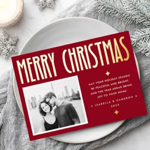 Horizontal custom photo holiday greeting card with a dark red background, featuring a tall gold foil Merry Christmas header, a white picture frame on the left, and editable white message typography with gold star foil accents on the right.