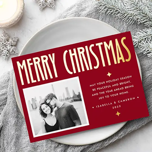 Horizontal custom photo holiday greeting card with a dark red background, featuring a tall gold foil Merry Christmas header, a white picture frame on the left, and editable white message typography with gold star foil accents on the right.