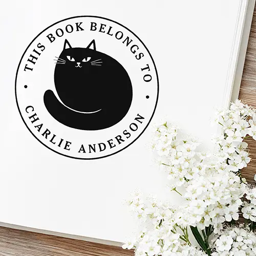 Round Ex Libris rubber stamp design showing a central black cat silhouette surrounded by a circular frame with text reading This Book Belongs To and a custom name.