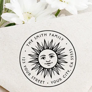 Round rubber stamp design featuring a central vintage sun face with radiant rays, surrounded by arched custom uppercase name and address text within a circular border.