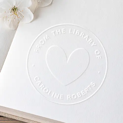 Round embossed seal featuring a central heart icon enclosed by a circular border and custom curved owner text.