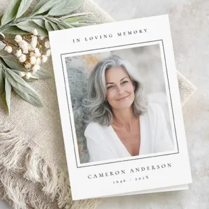 Vertical white folded memorial card displaying a line framed portrait on the front cover above centered serif name and date typography.