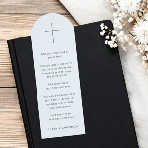 Arched paper bookmark in soft light blue featuring a dark cross icon at the top, italicized body text, and a dark uppercase name at the bottom.