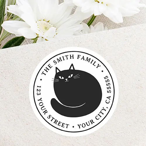 Round white self-adhesive return address label featuring a central illustrated black cat curled up with circular black serif text along the inner border.