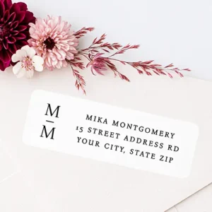 Rectangular white return address label with black stacked monogram A white rectangular rounded-corner sticker displaying a stacked two-letter monogram with a divider line on the left, alongside three lines of black serif address text on the right.