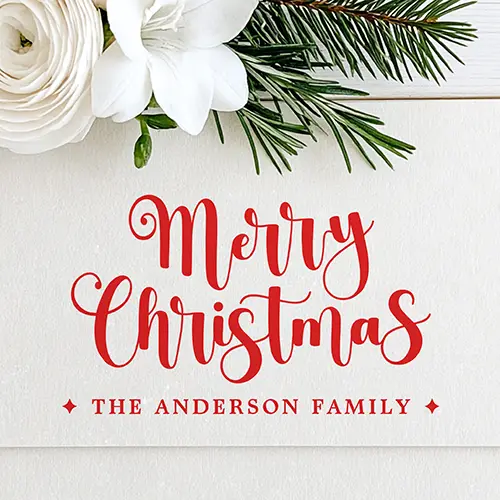Wooden rubber stamp design showing a cursive Merry Christmas script above a custom serif family name line flanked by diamond accents.