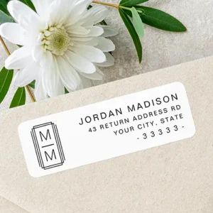 Minimalist monogram white return address label A white rectangular address sticker with rounded corners featuring a black geometric Art Deco monogram frame on the left and right-aligned black text on the right.