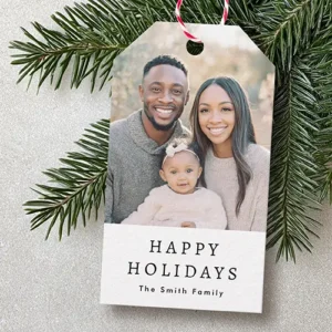 Vertical gift tag with angled top corners featuring a family portrait on top and elegant text reading Happy Holidays with a custom family name on a white base.