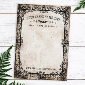 A rectangular double-sided earring holder card featuring an ornate black filigree border on aged parchment paper with custom business text and a distressed dark back side.