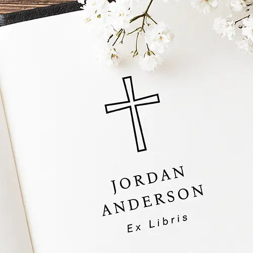 Religious bookplate rubber stamp featuring a central Christian cross icon centered over customizable serif name template fields.